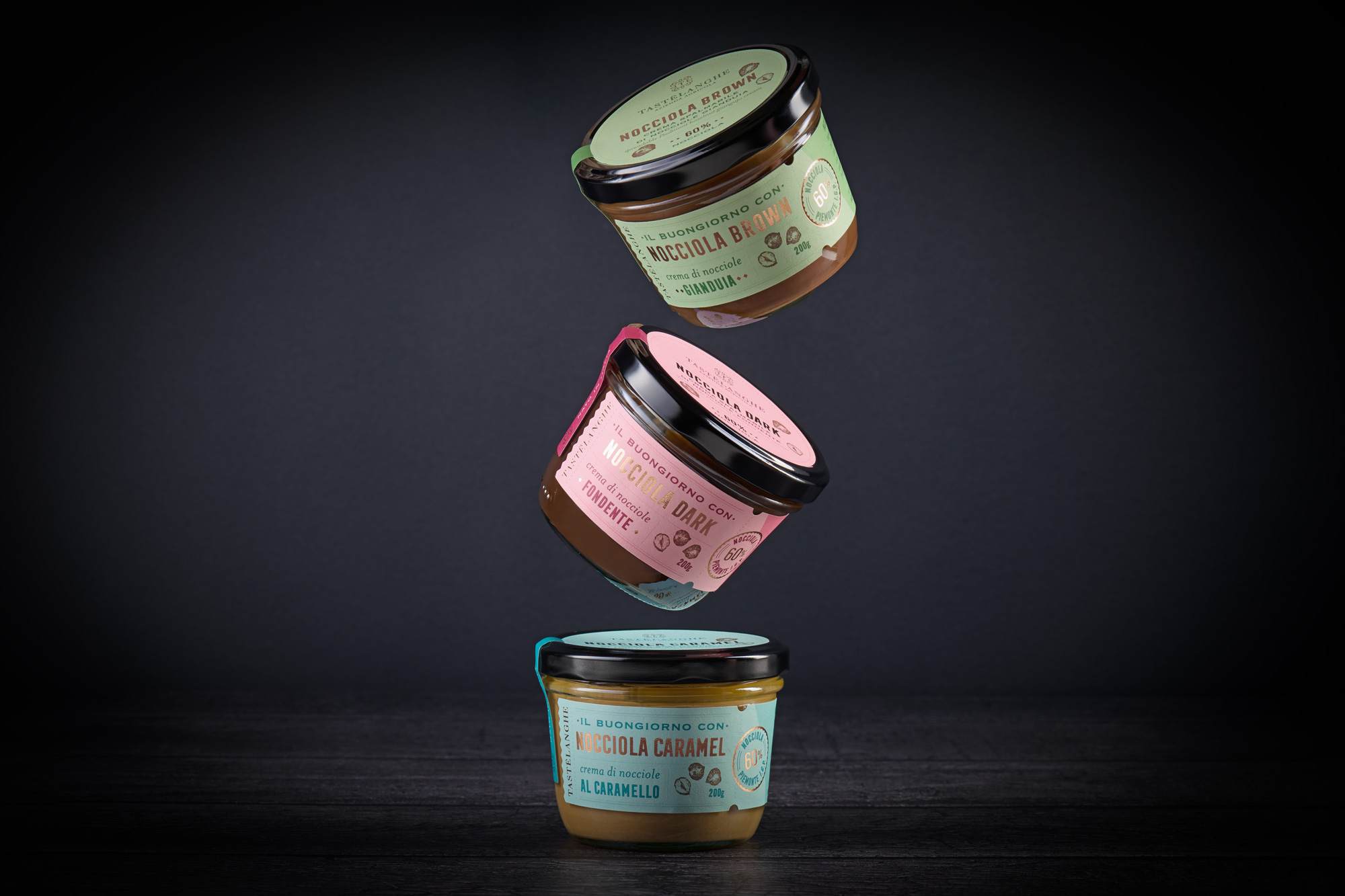 Tre barattoli di crema di nocciole Tastelanghe in sospensione su fondo scuro, fotografia di packaging in vetro con etichette in lamina